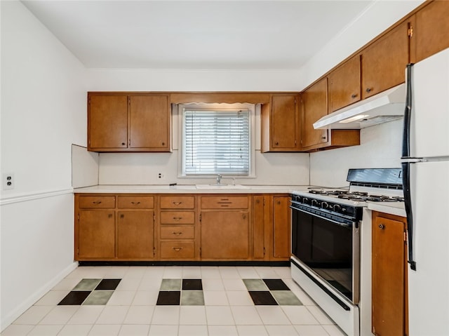 kitchen with gas range, a sink, light countertops, freestanding refrigerator, and under cabinet range hood