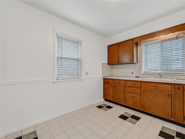 kitchen with brown cabinetry, a sink, baseboards, and light countertops