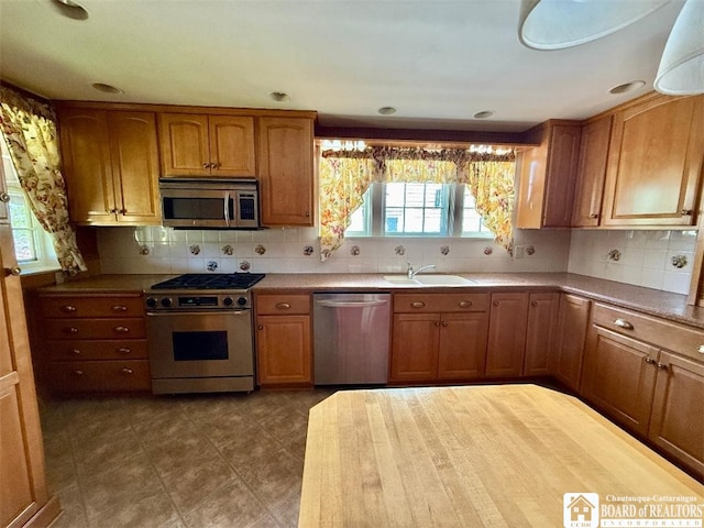 148 Myrtle St, Jamestown, NY 14701 - kitchen featuring brown cabinetry, appliances with stainless steel finishes, tasteful backsplash, a sink, and dark tile patterned flooring
