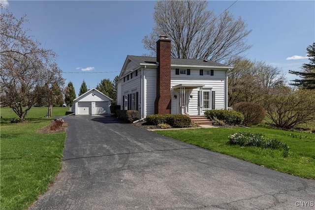 colonial inspired home featuring a chimney, an outbuilding, a front yard, and a garage