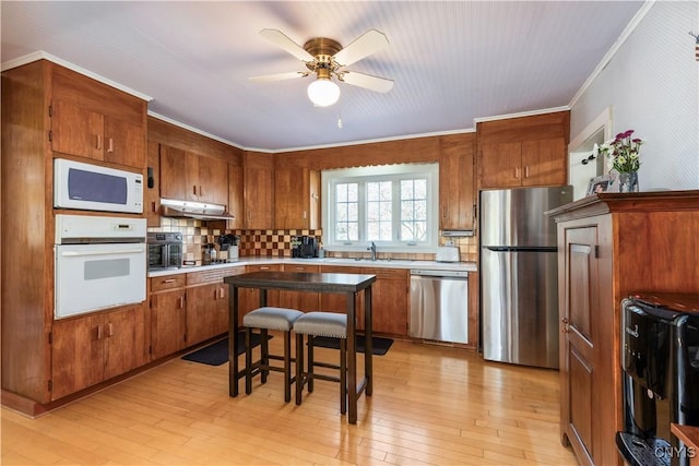 kitchen with crown molding, appliances with stainless steel finishes, brown cabinetry, and a ceiling fan