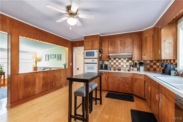 kitchen with brown cabinetry, light wood-type flooring, a sink, light countertops, and white appliances