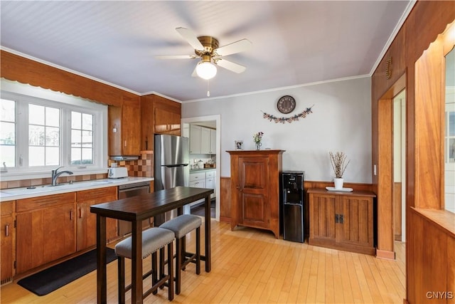 kitchen featuring brown cabinetry, ceiling fan, light countertops, a sink, and stainless steel appliances