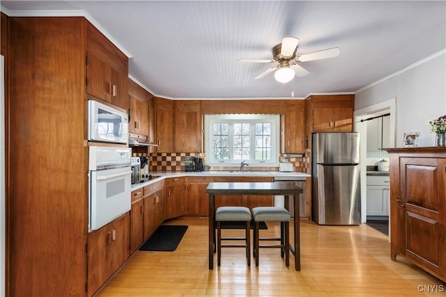 kitchen with light wood finished floors, stainless steel appliances, a ceiling fan, decorative backsplash, and under cabinet range hood