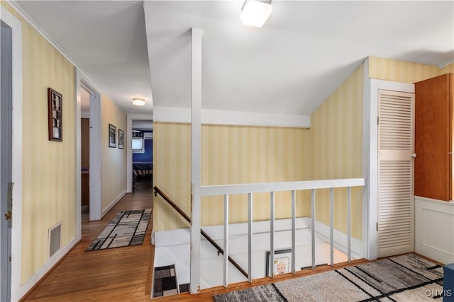 hallway featuring visible vents, wood finished floors, baseboards, wallpapered walls, and an upstairs landing