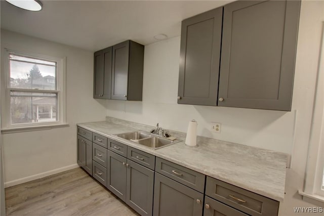 kitchen with light countertops, gray cabinets, a sink, and light wood-style flooring