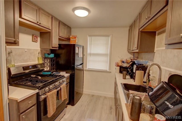 kitchen with a sink, stainless steel gas stove, light countertops, baseboards, and light wood-type flooring