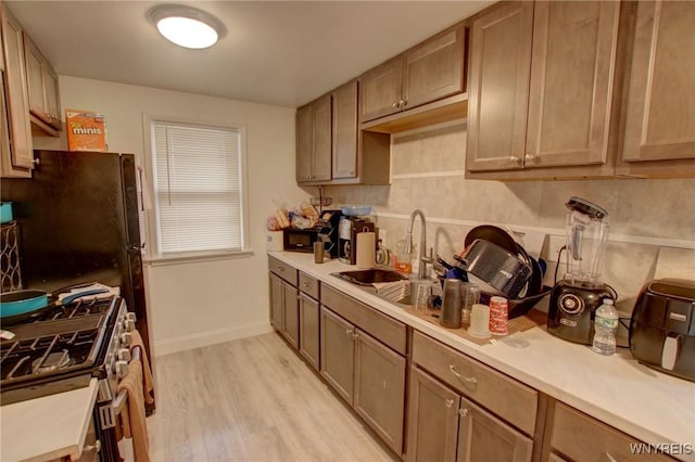 kitchen with a sink, gas stove, light wood-style floors, light countertops, and baseboards