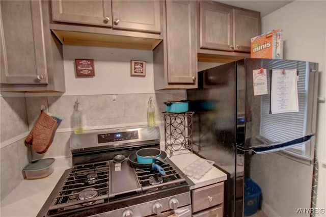 kitchen with light countertops, stainless steel range with gas stovetop, tasteful backsplash, and freestanding refrigerator