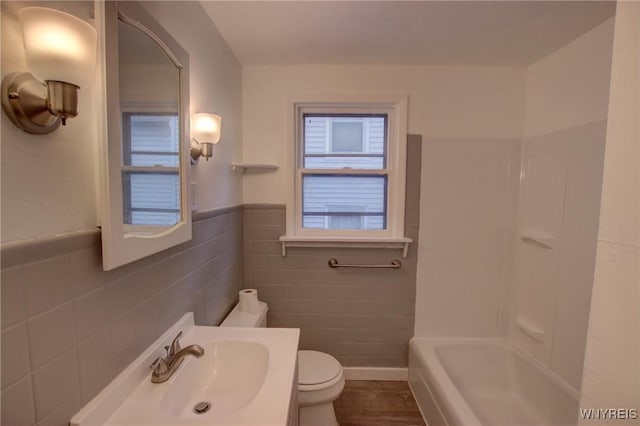 bathroom with vanity, wainscoting, bathing tub / shower combination, toilet, and tile walls