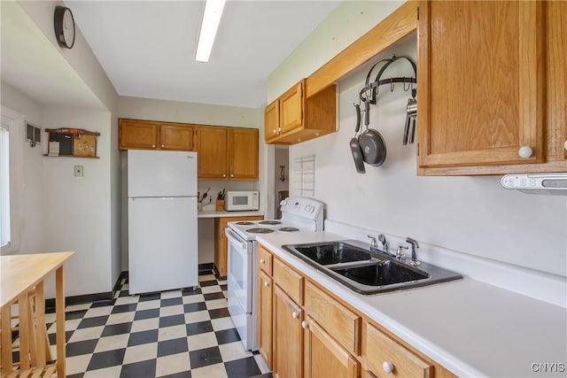 kitchen featuring brown cabinets, a sink, white appliances, light countertops, and dark floors