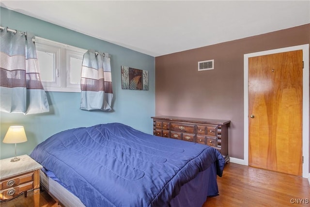 bedroom with baseboards, visible vents, and wood finished floors