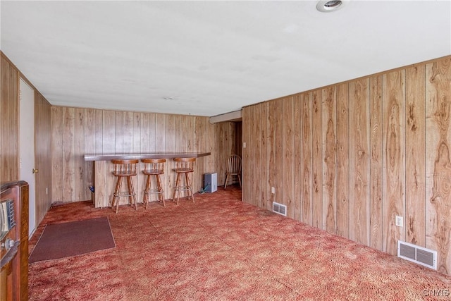 carpeted empty room featuring visible vents, a dry bar, and wood walls