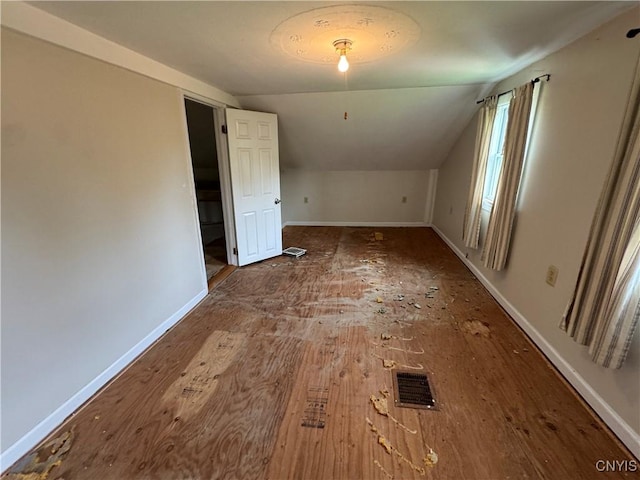 additional living space with baseboards, visible vents, wood finished floors, and vaulted ceiling
