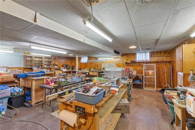 misc room featuring wooden walls, a workshop area, concrete floors, and a drop ceiling