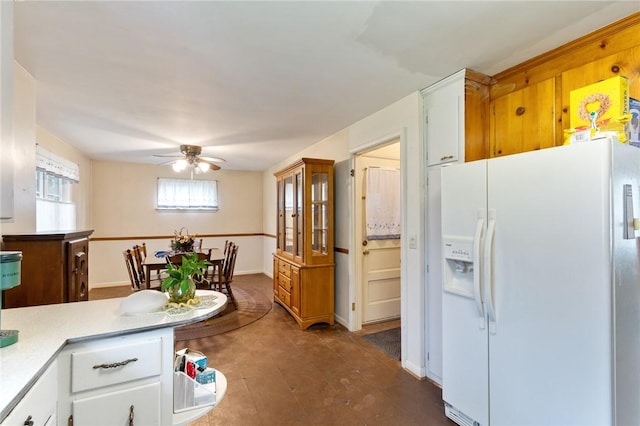 kitchen with light countertops, white fridge with ice dispenser, a ceiling fan, baseboards, and white cabinetry