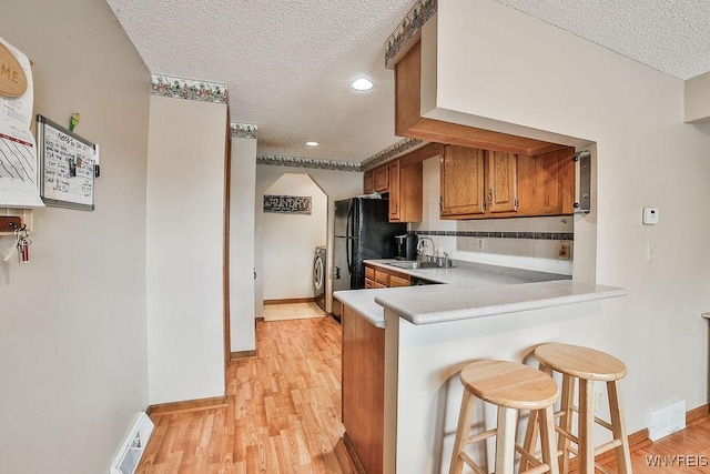 kitchen featuring visible vents, a breakfast bar, a textured ceiling, brown cabinets, and a sink