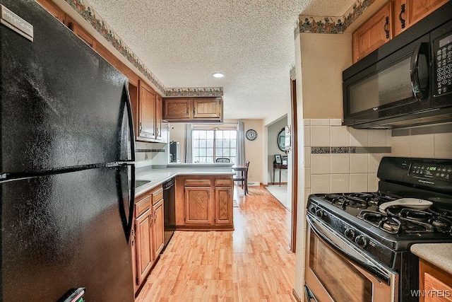 kitchen featuring a textured ceiling, light wood finished floors, brown cabinets, and black appliances