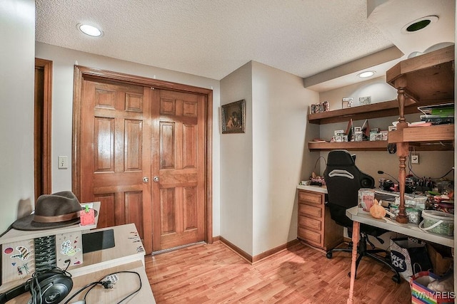 office area with light wood-style floors, baseboards, built in study area, and a textured ceiling