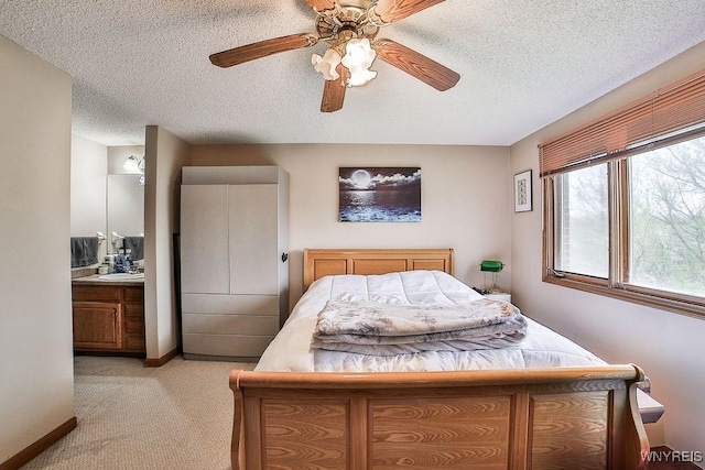 bedroom with ceiling fan, light carpet, ensuite bath, and a textured ceiling
