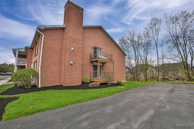 view of side of home with brick siding, a chimney, and a balcony