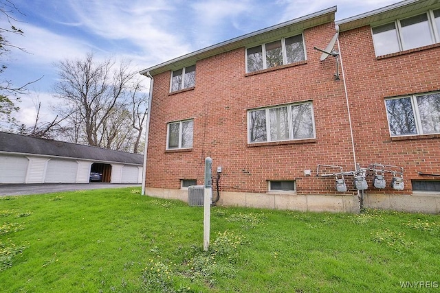 view of side of property featuring a lawn, central AC unit, brick siding, and a detached garage