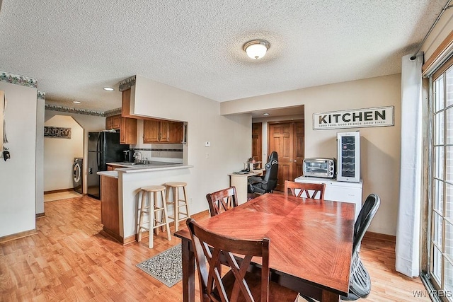 dining space featuring light wood-type flooring, a textured ceiling, washer / clothes dryer, and baseboards