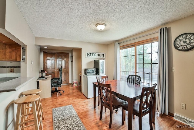 dining space with a toaster, light wood-type flooring, a textured ceiling, and visible vents