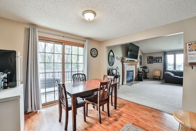 dining room featuring a tiled fireplace, a textured ceiling, and light wood finished floors