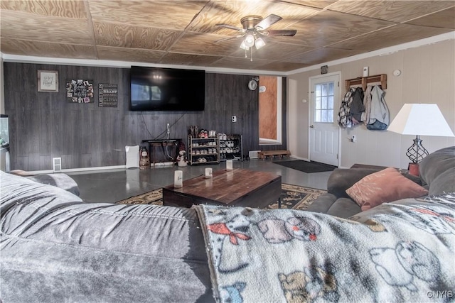 living room featuring baseboards, wood walls, ceiling fan, and an ornate ceiling