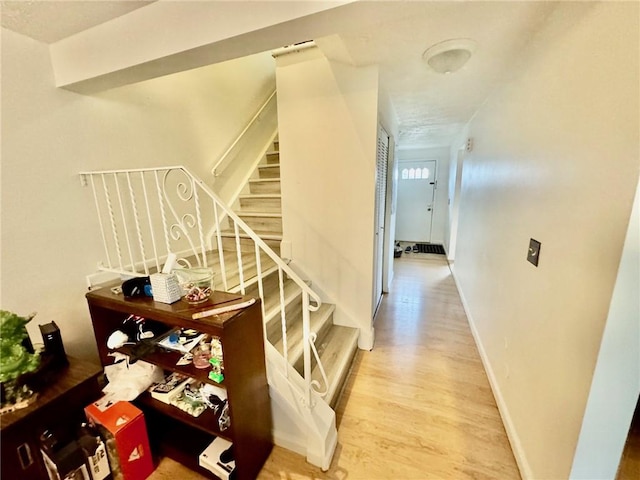 corridor featuring baseboards, light wood-style flooring, and stairs