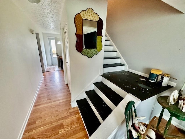 hallway featuring baseboards, a textured ceiling, wood finished floors, and stairway