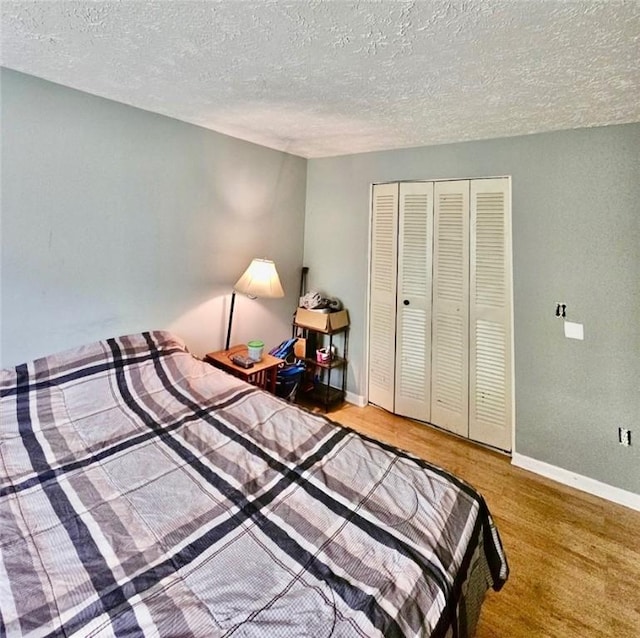 bedroom featuring a closet, a textured ceiling, baseboards, and wood finished floors