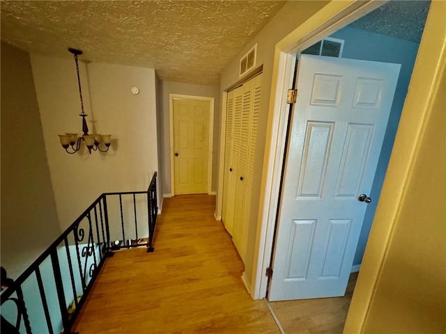 hallway with a chandelier, wood finished floors, visible vents, and an upstairs landing