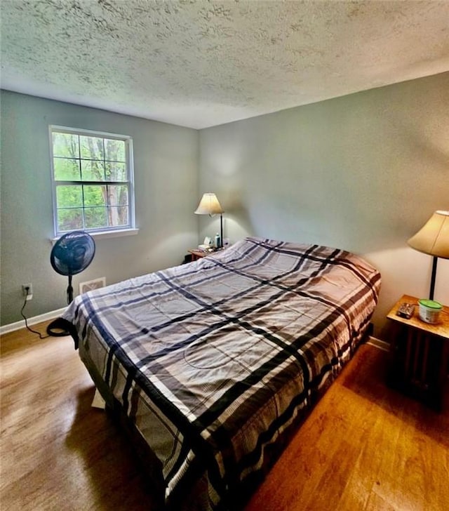 bedroom with a textured ceiling, baseboards, and wood finished floors