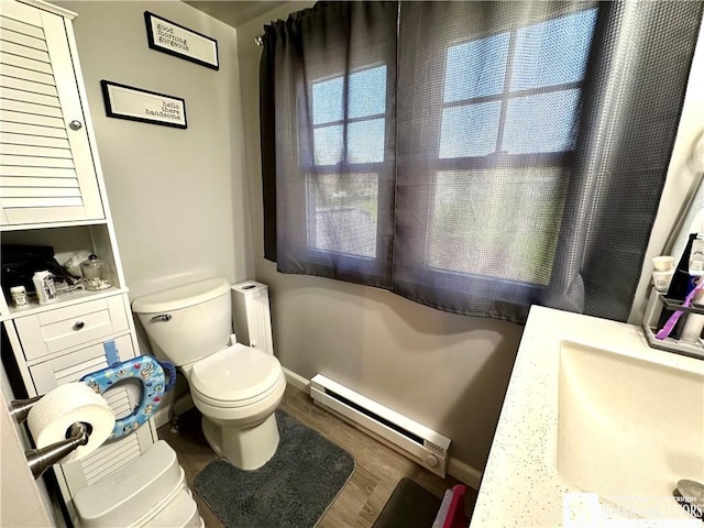 bathroom featuring wood finished floors, toilet, baseboards, baseboard heating, and a sink
