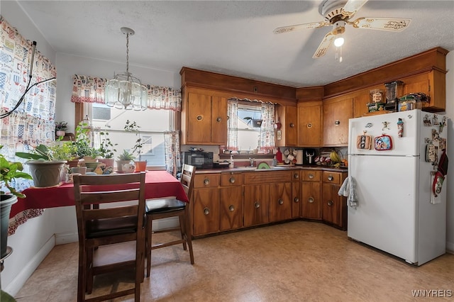 kitchen with dark countertops, freestanding refrigerator, ceiling fan with notable chandelier, and brown cabinetry