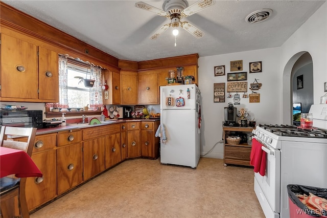 kitchen featuring ceiling fan, arched walkways, brown cabinets, a sink, and white appliances