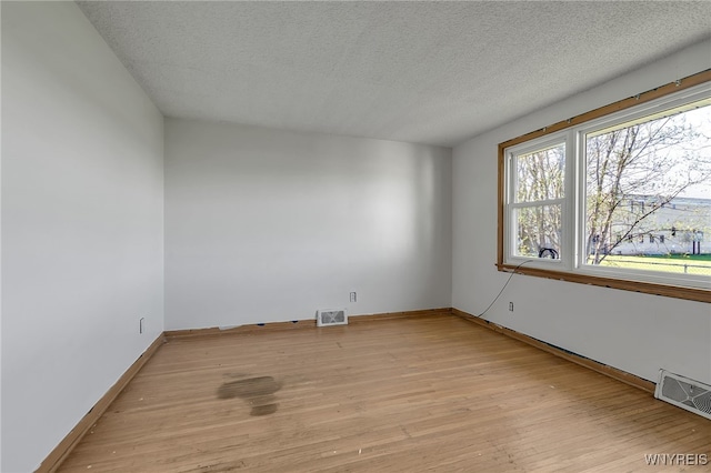 unfurnished room with a textured ceiling, visible vents, and light wood-style floors