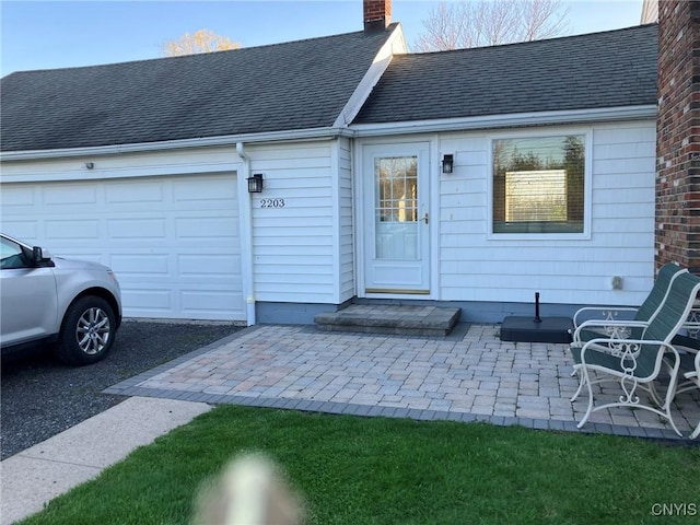 property entrance with roof with shingles, a chimney, and an attached garage