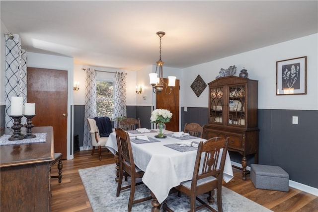 dining area featuring an inviting chandelier, wood finished floors, and a wainscoted wall