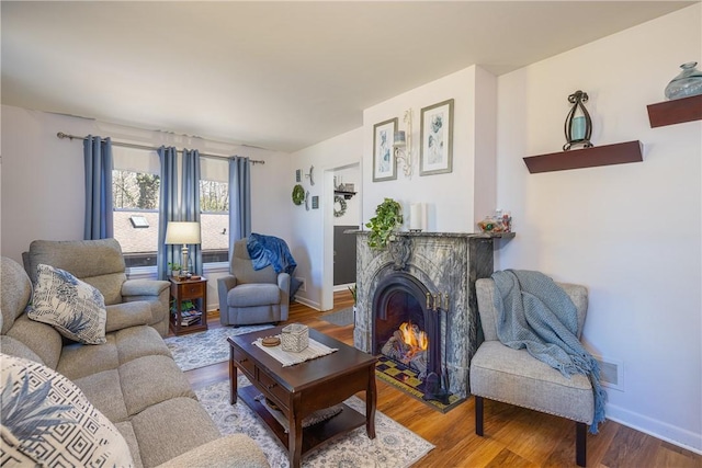 living room featuring baseboards, wood finished floors, and a lit fireplace