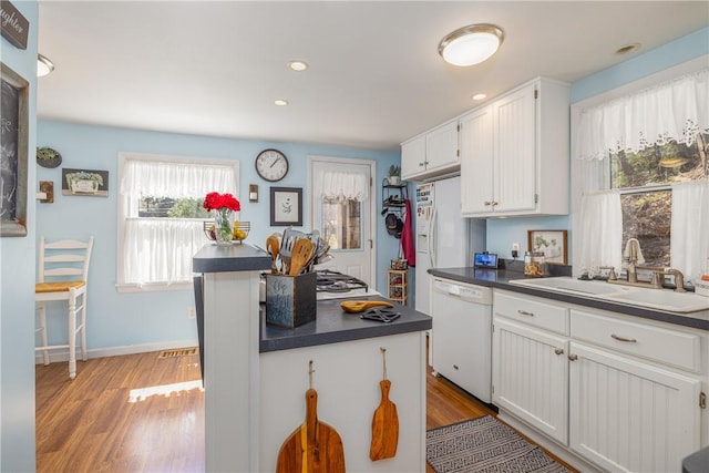kitchen with a sink, light wood finished floors, dishwasher, and dark countertops