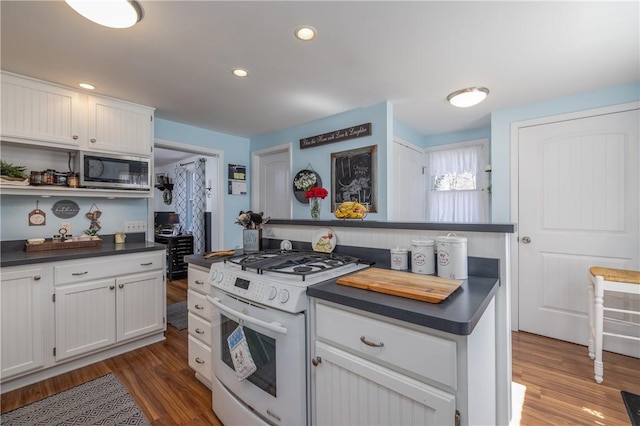 kitchen featuring dark countertops, white gas stove, stainless steel microwave, and white cabinetry