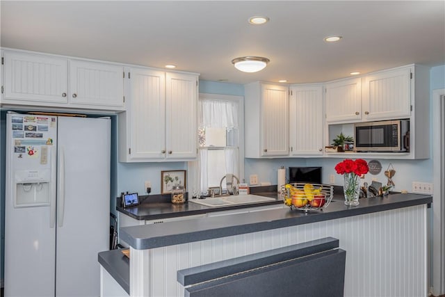 kitchen featuring white cabinetry, stainless steel microwave, white refrigerator with ice dispenser, and dark countertops