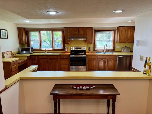 kitchen featuring recessed lighting, light countertops, under cabinet range hood, a sink, and stainless steel appliances