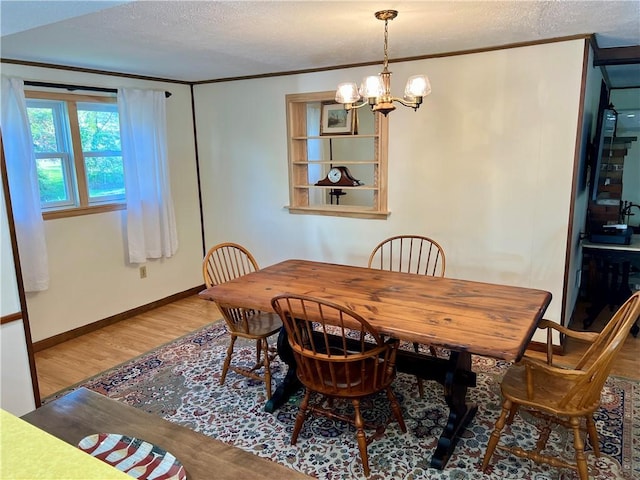 dining room with an inviting chandelier, a textured ceiling, baseboards, wood finished floors, and ornamental molding