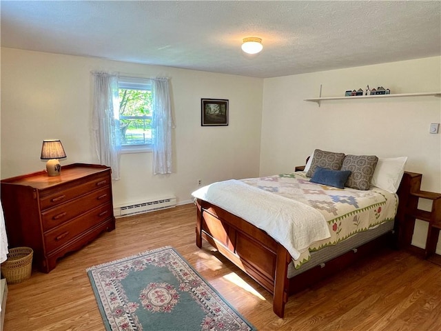 bedroom with light wood-type flooring, a textured ceiling, and a baseboard heating unit