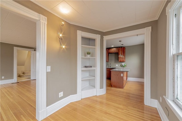 corridor featuring crown molding, baseboards, light wood finished floors, and stairs