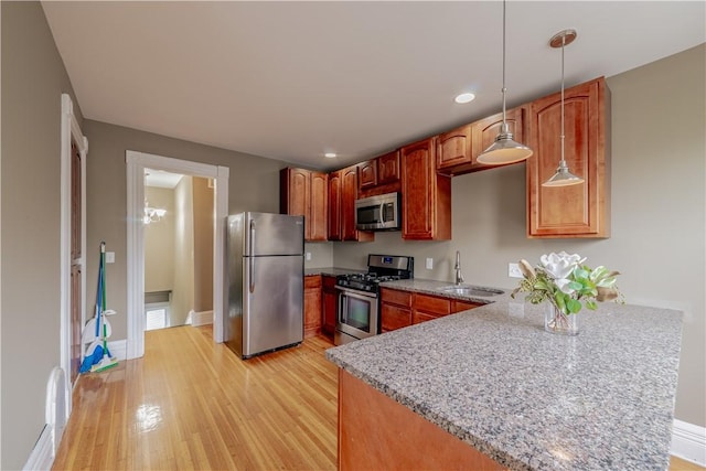 kitchen with appliances with stainless steel finishes, light stone counters, a sink, light wood-style flooring, and a peninsula